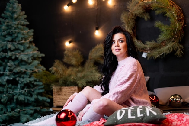 Hermosa mujer atractiva con árbol de Navidad en el fondo. Joven dama alegre en una cama con interior de vacaciones.