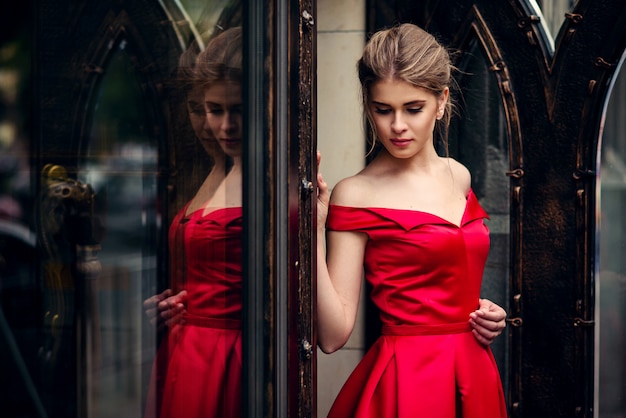 Hermosa mujer atractiva en un vestido rojo de pie junto a la puerta de metal forjado