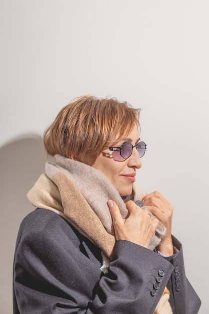 Hermosa mujer baby boomer de mediana edad con gafas de sol sonriendo y mirando hacia otro lado fondo gris claro