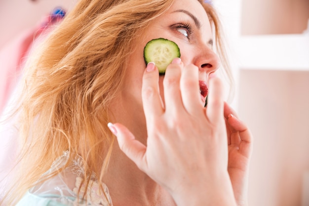 Foto una hermosa mujer con una bata y rodajas de pepino en el rostro se encuentra frente al espejo