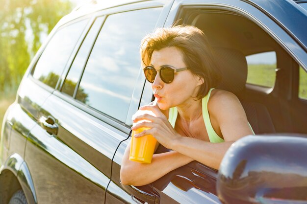 Hermosa mujer bebiendo jugo, sentado en su auto