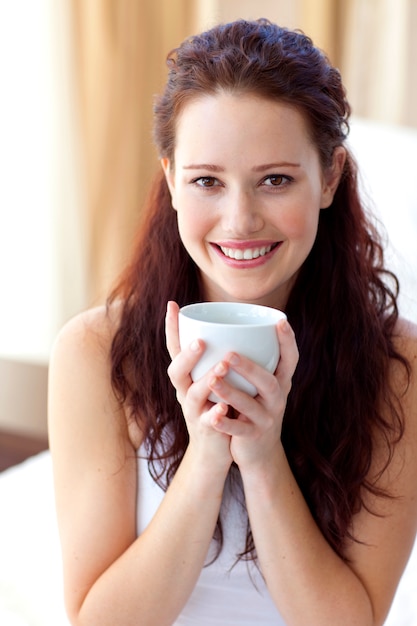 Hermosa mujer bebiendo una taza de café en el dormitorio