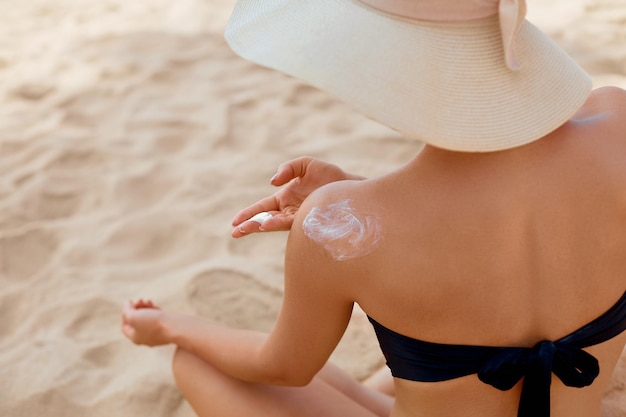 Hermosa mujer en bikini aplicando crema solar en la protección solar del hombro bronceado