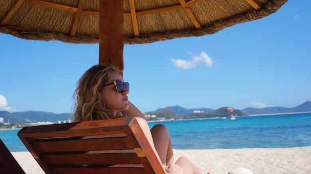 Hermosa mujer en bikini disfruta del sol tropical para broncearse en una tumbona en una playa tropical en China