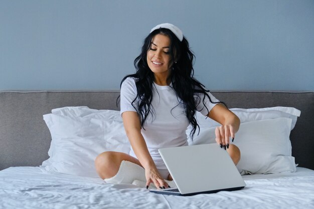 Hermosa mujer blogger sentada en la cama con computadora portátil, mujer con peinado maquillaje blog de belleza líder para mujeres y niñas