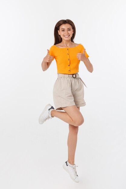 Hermosa mujer con blusa naranja saltando y mostrando los pulgares para arriba