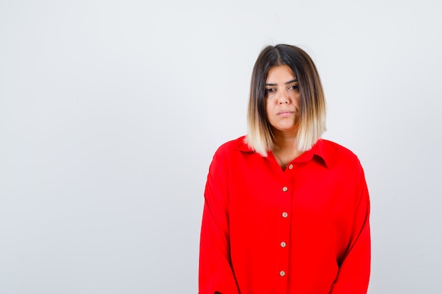 Hermosa mujer en blusa roja mirando a cámara y mirando seria, vista frontal.