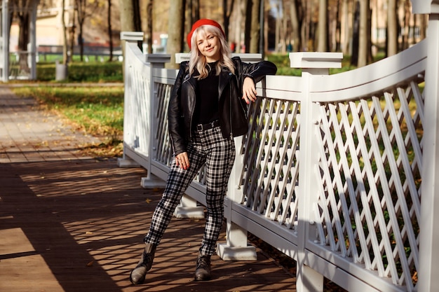 Hermosa mujer de boina roja, chaqueta de cuero negro, pantalones a cuadros pasar tiempo al aire libre en otoño