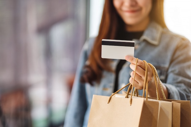 Una hermosa mujer con bolsas de compras sosteniendo y usando una tarjeta de crédito para comprar