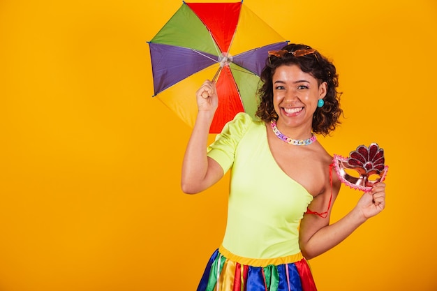 Foto hermosa mujer brasileña afroamericana en ropa de carnaval animando con colorida sombrilla y máscara de carnaval