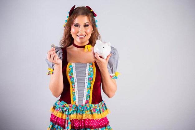 Hermosa mujer brasileña con ropa de campo Festa de Sao Joao Festa Junina sosteniendo alcancía y economía de monedas finanzas