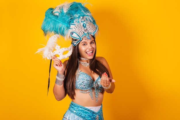 Hermosa mujer brasileña con ropa de carnaval azul y blanca con corona de plumas y máscara invitando al carnaval