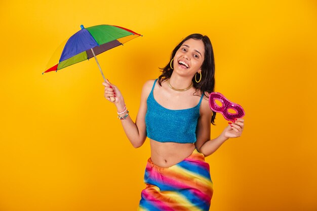 Hermosa mujer brasileña en ropa de carnaval con paraguas colorido y máscara de carnaval