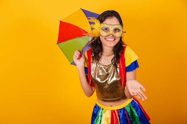 Hermosa mujer brasileña en ropa de carnaval con ropa de frevo y colorido paraguas y máscara de bienvenida