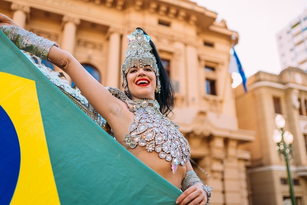 Hermosa mujer brasileña vistiendo coloridos trajes de carnaval y la bandera de Brasil durante el desfile de Carnaval en la ciudad.