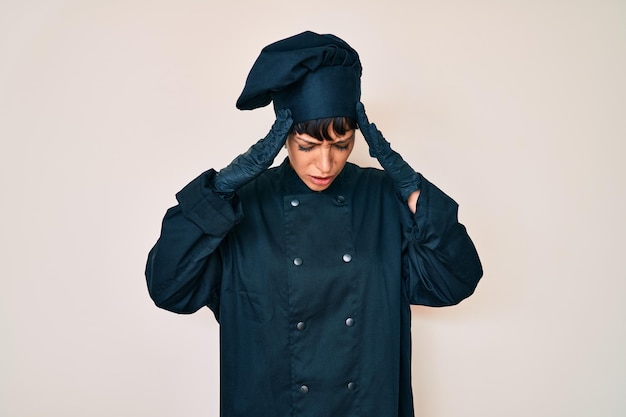 Hermosa mujer brunettte con uniforme de cocinera profesional con la mano en la cabeza por dolor en la cabeza porque el estrés sufre migraña