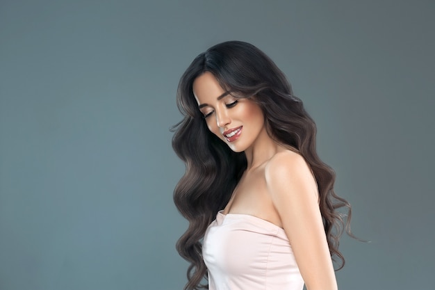 Hermosa mujer con cabello largo, brillo y rizado, mujer de niña de belleza sobre fondo gris darl. Tiro del estudio.