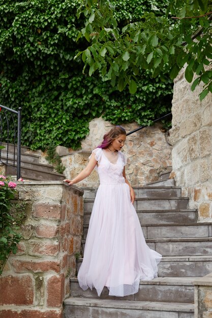 Hermosa mujer con cabello morado con un vestido de novia blanco camina en el jardín. Maquillaje natural