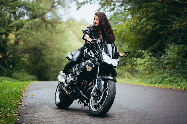 Hermosa mujer, con cabello negro y rizado, con una chaqueta de cuero negro, sentada en una motocicleta deportiva