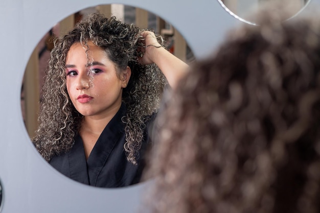 Hermosa mujer con cabello rizado posa y cambia su peinado mientras se mira en el espejo