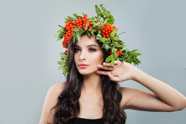 Hermosa mujer con cabello rizado saludable y maquillaje natural con bayas rojas y corona de hojas verdes