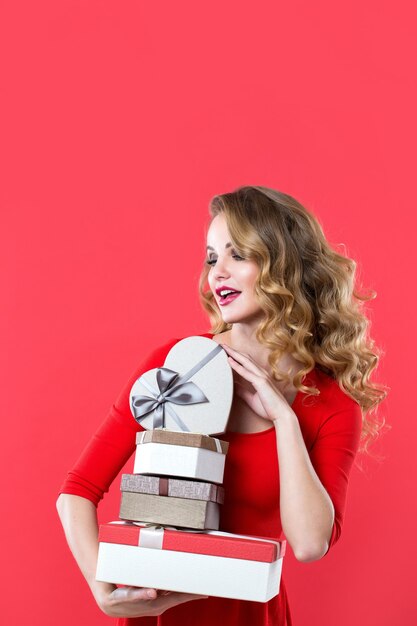 Hermosa mujer con cabello rizado sosteniendo muchas cajas sobre fondo rojo.