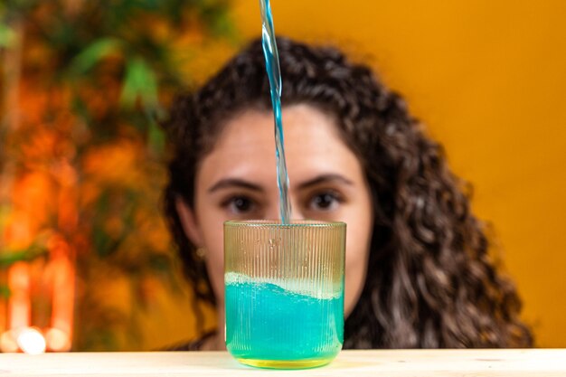 Foto una hermosa mujer de cabello rizado está viendo una salpicadura de refresco azul caer en un vaso