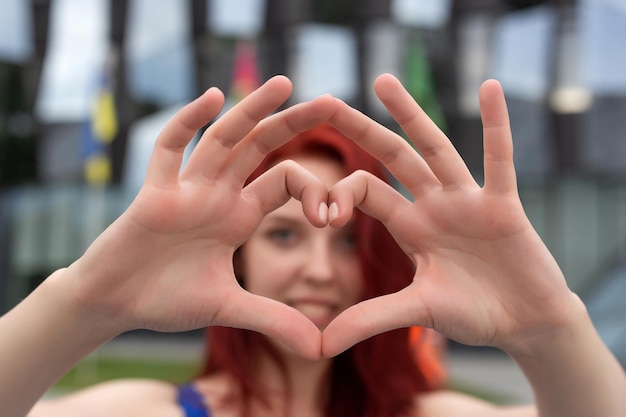 Hermosa mujer con cabello rojo hace manos de un corazón y lo muestra Retrato de una mujer joven al aire libre