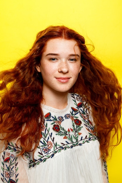Hermosa mujer con cabello rojo ondulado sobre fondo amarillo