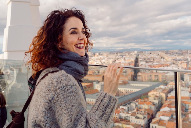 Hermosa mujer de cabello rojo con una sonrisa alegre visitando el horizonte de Madrid desde la azotea de un hotel