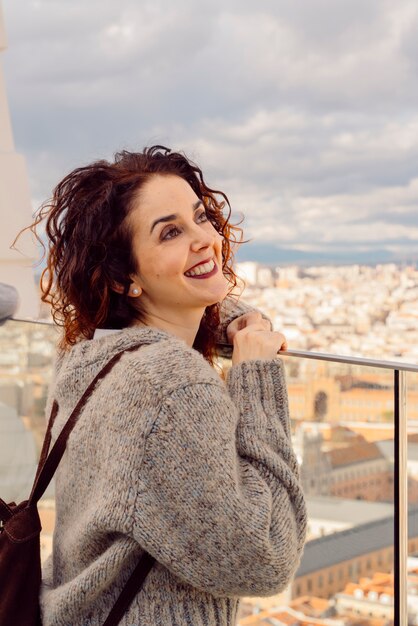 Hermosa mujer de cabello rojo con una sonrisa alegre visitando el horizonte de Madrid desde la azotea de un hotel