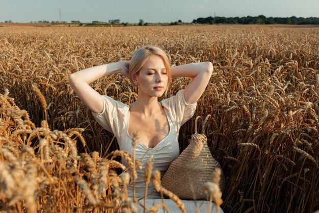 Hermosa mujer de cabello rubio con vestido blanco se sienta en el campo de trigo