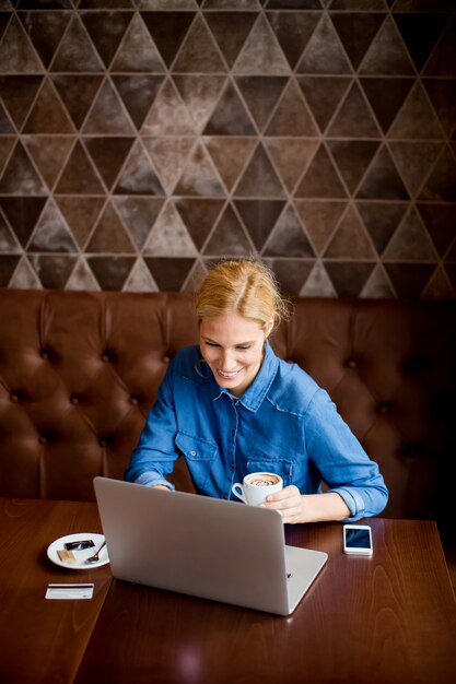 Hermosa mujer en el café con la computadora portátil con un descanso para tomar café