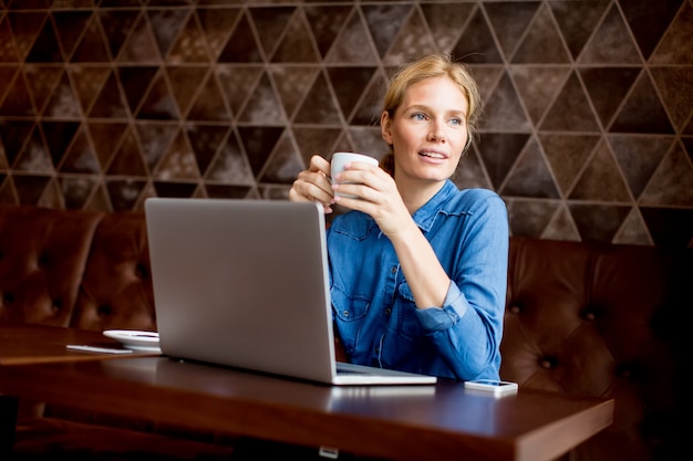 Hermosa mujer en el café con la computadora portátil con un descanso para tomar café