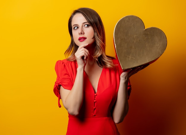 Hermosa mujer con caja en forma de corazón en la pared amarilla