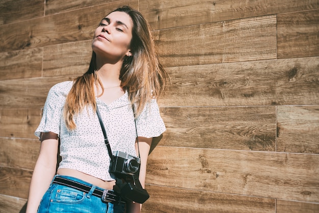 Hermosa mujer con cámara antigua vintage de pie en una pared de madera