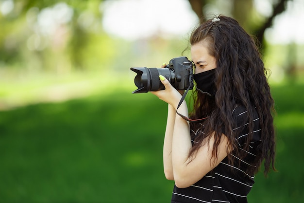 Hermosa mujer con una cámara usa una máscara médica y toma fotos en el parque