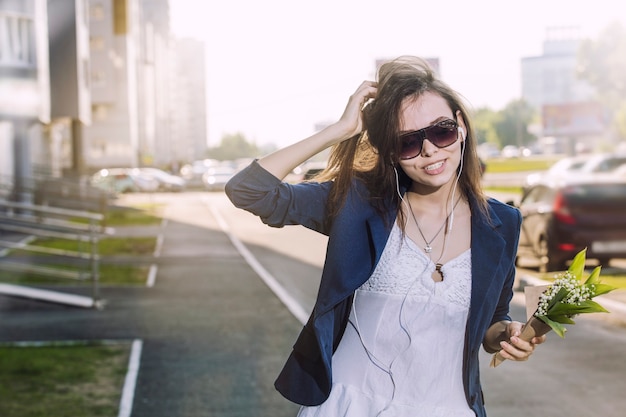 Hermosa mujer camina por la ciudad escuchando música en auriculares con un ramo de lirios en sus manos