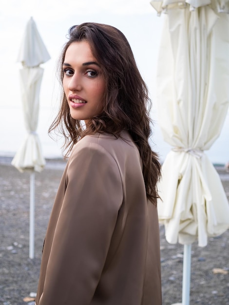 hermosa mujer caminando a lo largo de la costa morena en chaqueta beige contra el fondo del mar