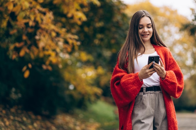 Hermosa mujer caminando en el parque de otoño y usando el teléfono