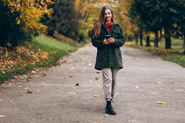 Hermosa mujer caminando en el parque de otoño y usando el teléfono