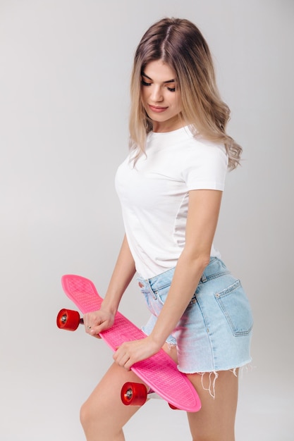 hermosa mujer en camiseta blanca con patineta rosa