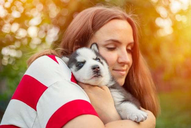 Una hermosa mujer con camiseta a rayas abraza tiernamente a un pequeño cachorro husky en el parque