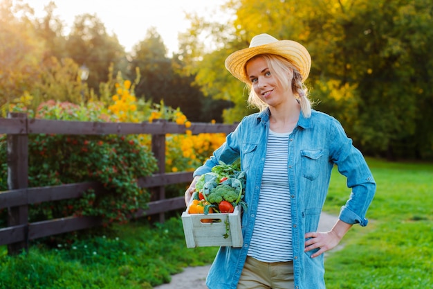 Hermosa mujer campesina en sombrero con caja de verduras ecológicas frescas