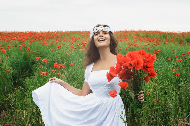 Hermosa mujer en campo con muchas flores de amapola