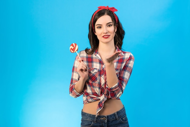 La hermosa mujer con un caramelo gesticulando sobre el fondo azul.