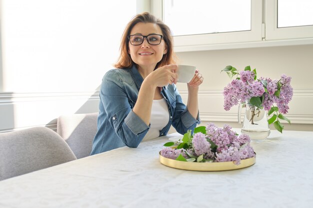 Hermosa mujer en casa con ramo de flores lilas