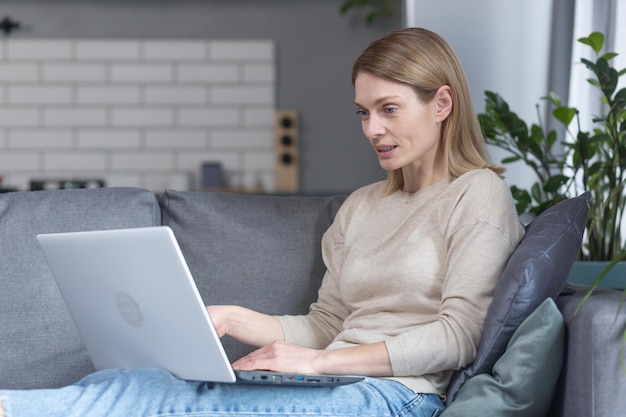 Hermosa mujer en casa sentada en un sofá sonriendo y trabajando en una laptop