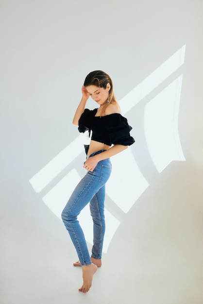 Hermosa mujer caucaisn joven delgada en blose negro y jeans sobre fondo blanco en estudio fotográfico