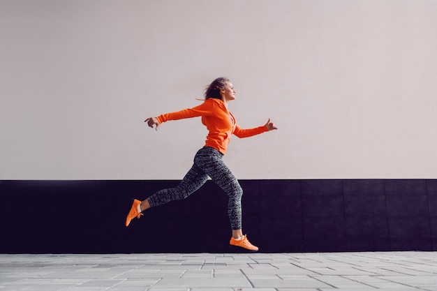 Hermosa mujer caucásica atractiva delgada en ropa deportiva y con el pelo rizado corriendo al aire libre.